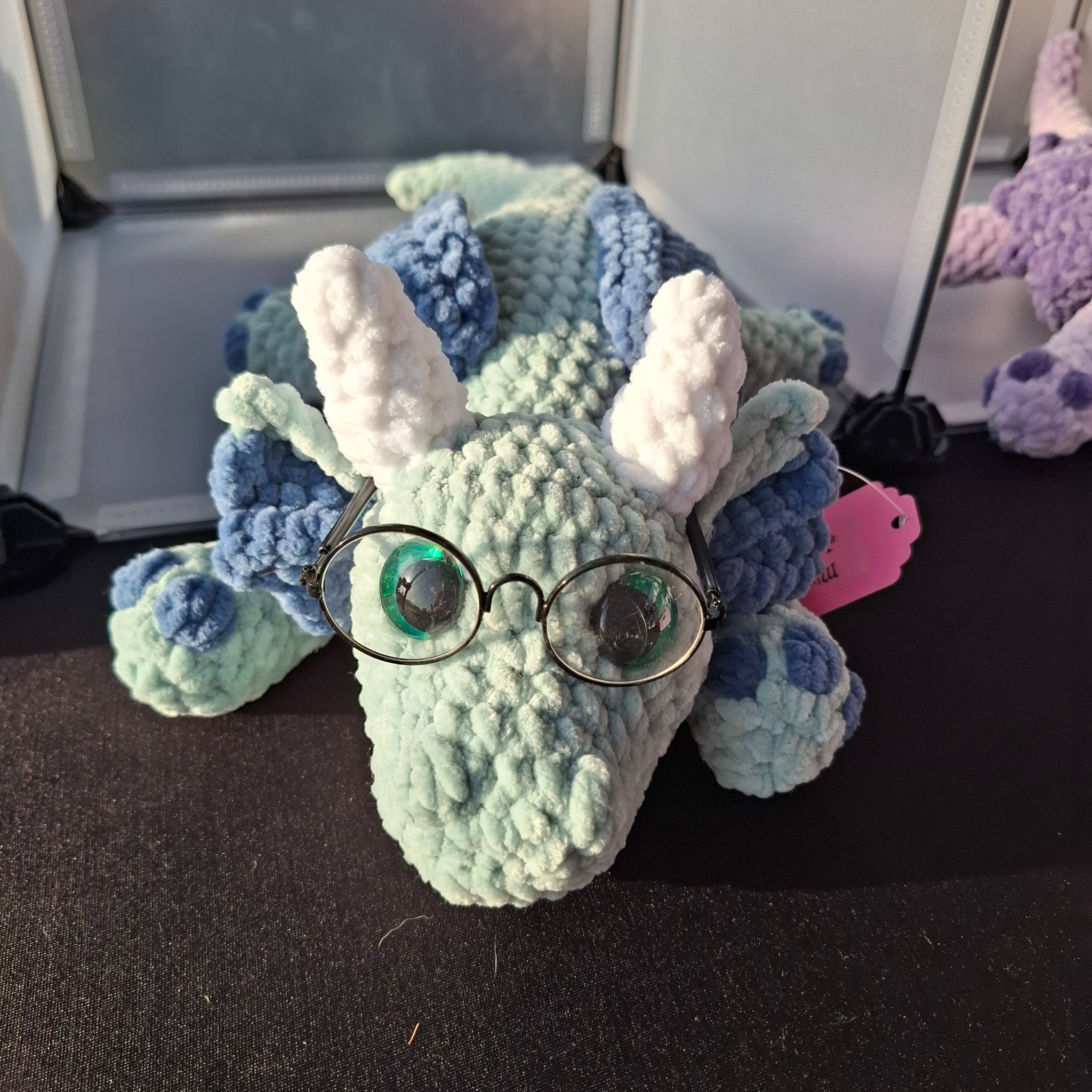 A mint and blue handmade crochet dragon wearing round glasses